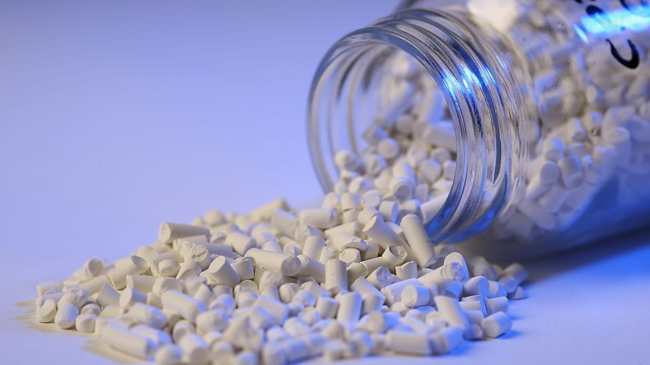 Catalyst product pouring out of a tipped glass bottle against a purple background.