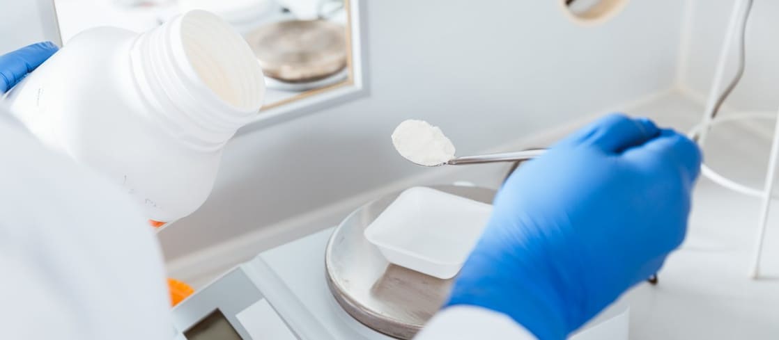 White lab environment with hand of a chemist in a blue safety glove